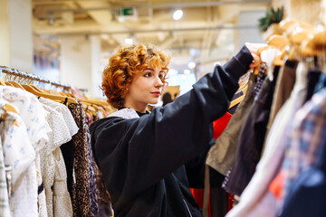 portrait of red-haired attractive young woman trying on clothes in store