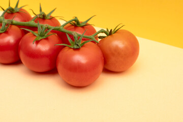 Red cherry tomatoes with green branch on yellow background