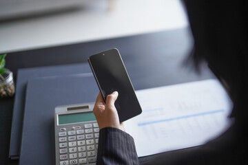 Asian businesswoman in suit holding smartphone and using pen writing on documents