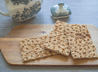 Crisp breads on a wooden cutting board, blue and white tea pot on a background, healthy snack