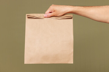 Close up cropped female hold in hand brown clear blank paper takeaway bag isolated on pastel plain...