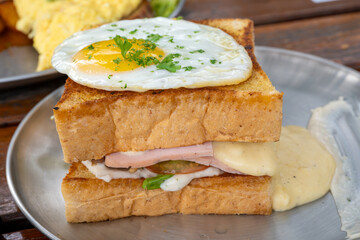 A delectable Croque Monsieur topped with a perfectly fried egg and garnished with fresh parsley. This classic French sandwich, featuring melted cheese and savory ham between slices of toasted bread.