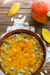 Orange pumpkin pie with dried seeds on a ceramic plate on a wooden table. Rustic style. Autumn mood. Tea time. Top view. Vertical orientation.