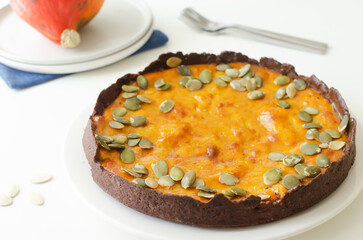 Orange pumpkin pie with dried seeds on a white plate on the table. Autumn mood. Tea time concept. Horizontal orientation