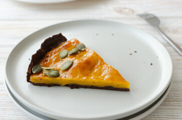 A piece of orange pumpkin pie with dried seeds on a white plate on the table. Autumn mood. Tea time concept. Horizontal orientation
