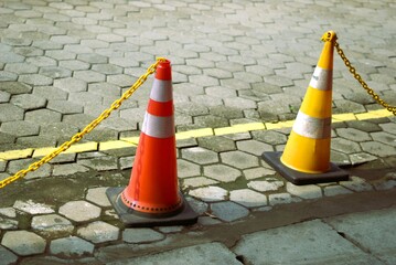 yellow and orange road cone with chain on a paving block