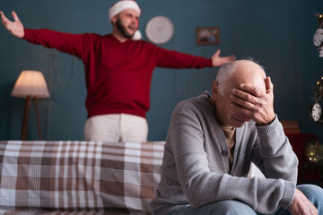 Fototapeta premium Young son arguing with elderly father sitting on the sofa in the living room. Family relationship problems