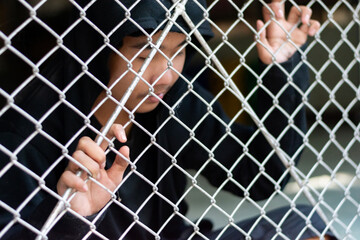 A young boy wearing a black hoody stands with his hands on a metal fence in a local detention...