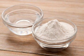 Baking soda in a glass bowl and mineral water in a glass bowl.
