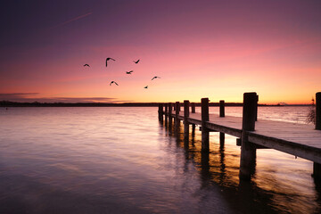 Fototapeta premium wooden pier over the calm sea, tranquil morning with beautiful sunrise, peaceful and quiet