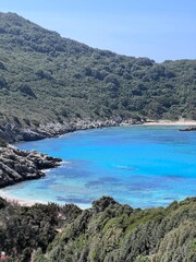 Fototapeta premium Beautiful summer panoramic seascape in Porto Timoni on the Greek island of Corfu. View from the rocky cliff to the crystal clear and azure sea bay and distant islands. A unique secluded beach. 