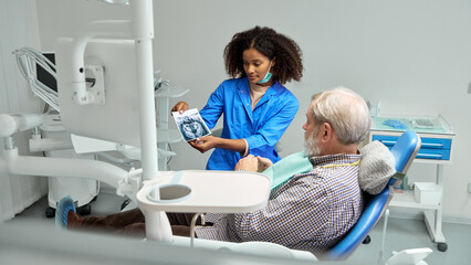 Dentist reviews X-ray image with mature man, patient, explaining details and preparing them for next steps in their dental care. Concept of health insurance, beauty, hygiene, dentist consultation. Ad.