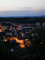 Fototapeta premium View of a warm-lit historic town under evening sky with distant hills and twinkling lights, captured during twilight hours