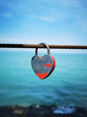 A heart-shaped padlock hanging on a rusted cable near serene blue waters in a tranquil seaside...
