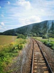 Scenic railway track winding through lush green fields and hills on a sunny day