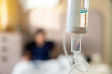 A person is hooked up to a drip in a hospital room. IV drip against patient blurred background in hospital.