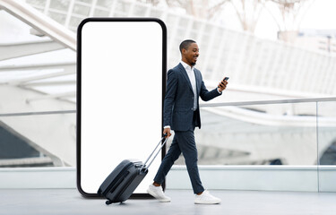 A well-dressed black man strolls through an airport terminal, wheeling a suitcase behind him and...