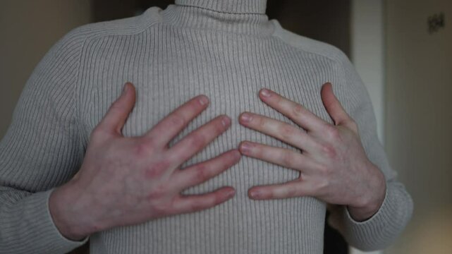 A man takes a deep, steadying breath, his hands raised slightly near his chest as if trying to calm himself. His expression and posture suggest concern, possibly reflecting on a patient's condition.