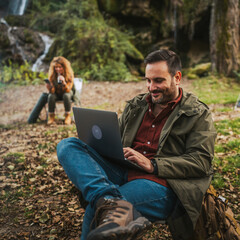 Fototapeta premium adult man hiker work remote on laptop in front waterfall and tent