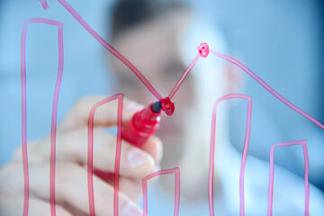 Businessman drawing bar graphs with red marker on transparent glass board