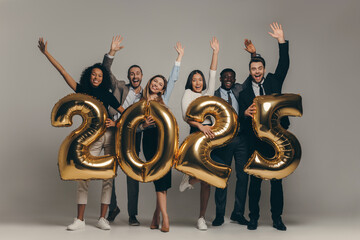 Group of happy business people holding 2025 numbers while celebrating New Year on studio background