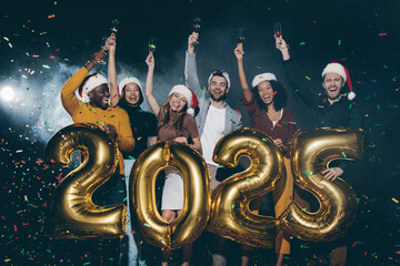 Group of happy young friends toasting with champagne while celebrating 2025 New Year in night club