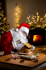 Jolly Santa Claus baking ginger bread, making ginger bread house. Warm and cozy festive room with fireplace, Christmas tree and twinkling lights. Coming holiday vibes