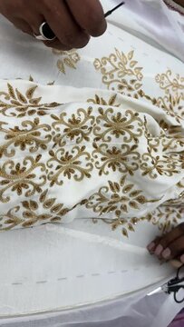 A Craftsman is doing hand embroidery on a white silk fabric, stretched in a wooden frame. Hand embroidery of a traditional motif with golden zari threads