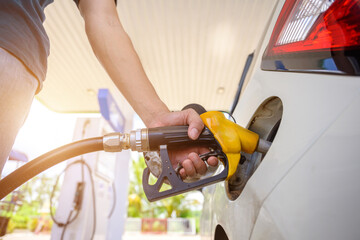 A close-up of a person using a yellow fuel nozzle to fill up their car at a gas station. of energy-related projects, the fuel industry, daily convenience, and transportation