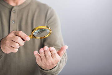 Man uses a magnifying glass to examine his palm, reflecting the practice of palmistry to enhance...