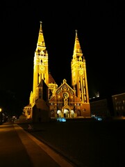 Stunning illuminated church towers at night in a peaceful town square showcasing Gothic...