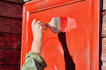 Flat paint brush 100 mm wide is used to paint front door of wooden farmhouse red.