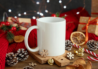 White coffee mug near red knitted sweater and Christmas decor and lights, winter mockup