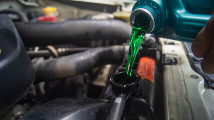Closeup of changing the coolant of a car radiator in the engine bay of a pickup truck. Emerald green oil poured from a gallon.
