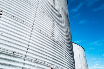Abstract view of large, metal grain storage and drying tanks seen at an agro business. Rivets and...