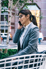 Fototapeta premium Cheerful businesswoman calling on cellphone at table in outdoors cafe