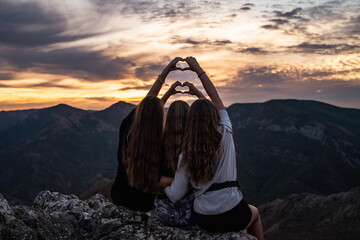 Tree happy female friends making heart shape with their hands with sunset in the background, sisters making a heart symbol in nature, friendship of young people, girl best friends at the sundown