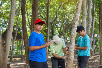 Asian boy taking notes on trees measured by friends to calculate the carbon storage of trees....