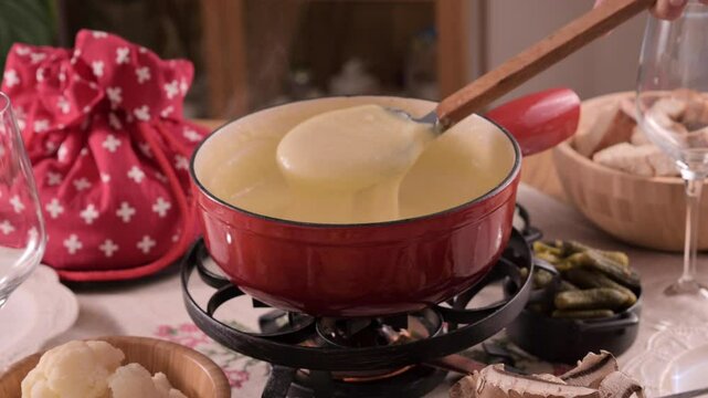 Cozy Swiss fondue setup with melted cheese, bread, pickles, and wine on a rustic table. advertising, social media campaigns, or food-related promotions. High quality 4k footage