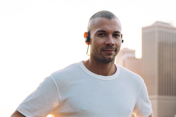 Happy jogger smiling in earphones in city embankment