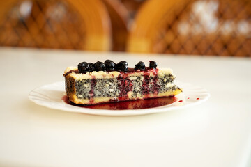 Closeup of delicious poppy seed crumble cheesecake with currant jam on a white round plate on a table, cottage cheese poppy seed pie, sweets bakery food deserts cuisine cafe concept