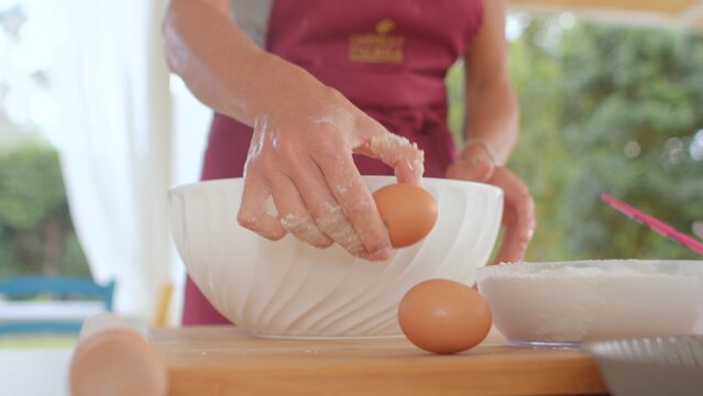 A woman is skillfully cracking eggs into a bowl that is placed on a wooden table