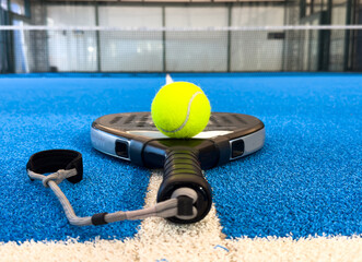 Black professional paddle tennis racket and ball with natural lighting on blue background....