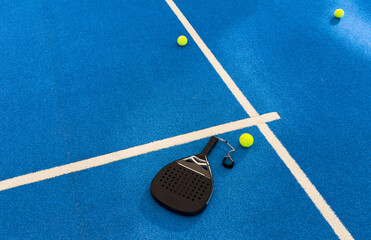 Black professional paddle tennis racket and ball with natural lighting on blue background....