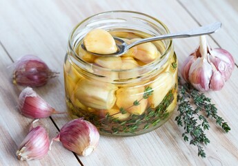 Spoon with garlic clove pickled in sunflower oil and thyme.  A glass jar full of garlic cloves should be kept in the refrigerator.