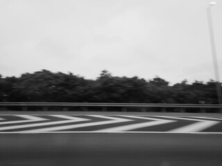 A desolate black-and-white highway stretches endlessly ahead, its empty lanes cutting through a...