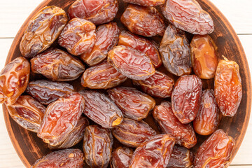 Obraz premium Several sweet dried pitted dates on a clay plate, macro, top view.