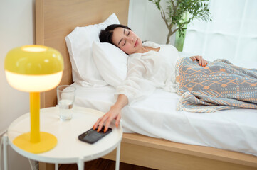 Sleeping asian woman turning off alarm on smartphone while being Waken up in the morning