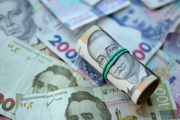 Roll of 500 Ukrainian Hryvnia money bills lies on big pile of ukrainian currency money close up