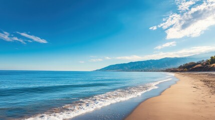 Obraz premium Serene beach with soft waves under a clear blue sky and distant hills.